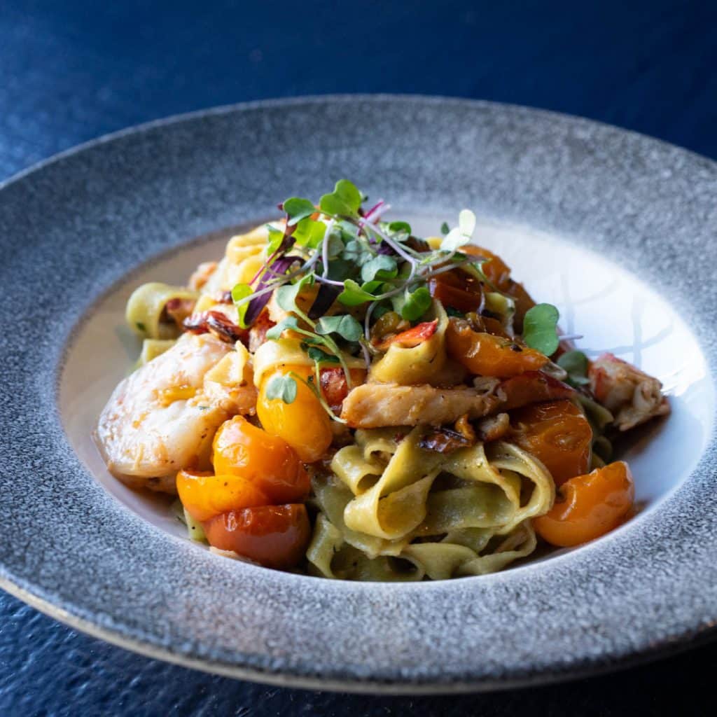 Plate of pasta with tagliatelle, cherry tomatoes, and grilled chicken, topped with microgreens on a textured gray plate